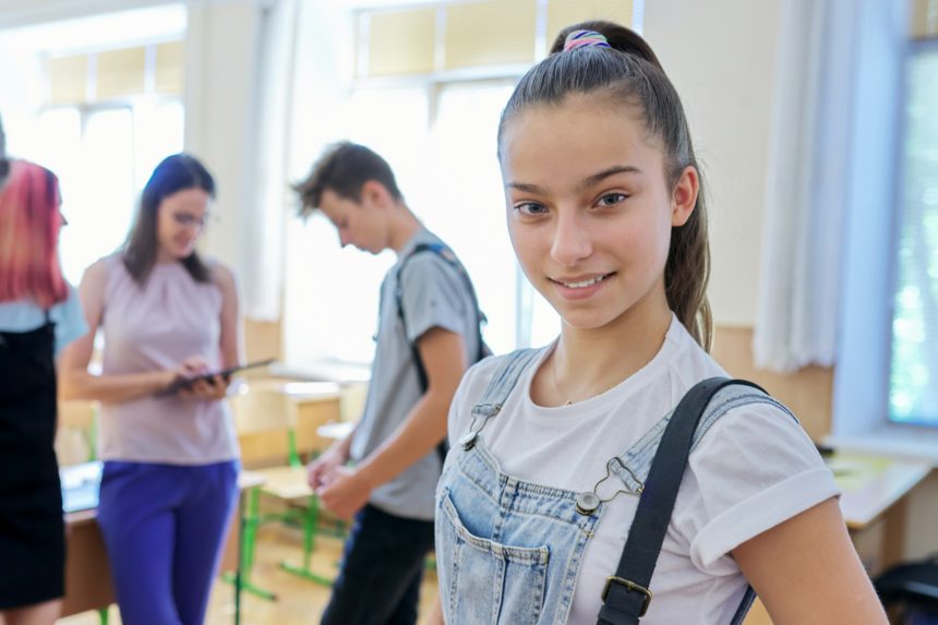 Portrait of teenage student girl in classroom with group of pupils and teacher